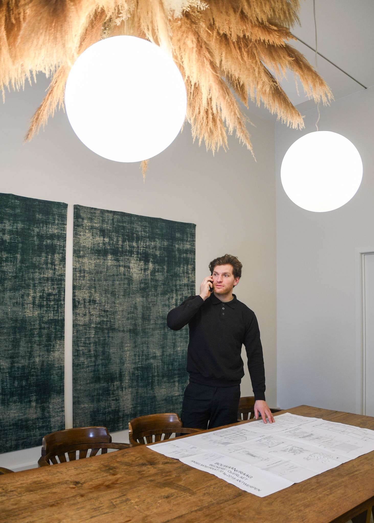 Maarten Dylst telefoneert aan een werktafel met bouwplannen